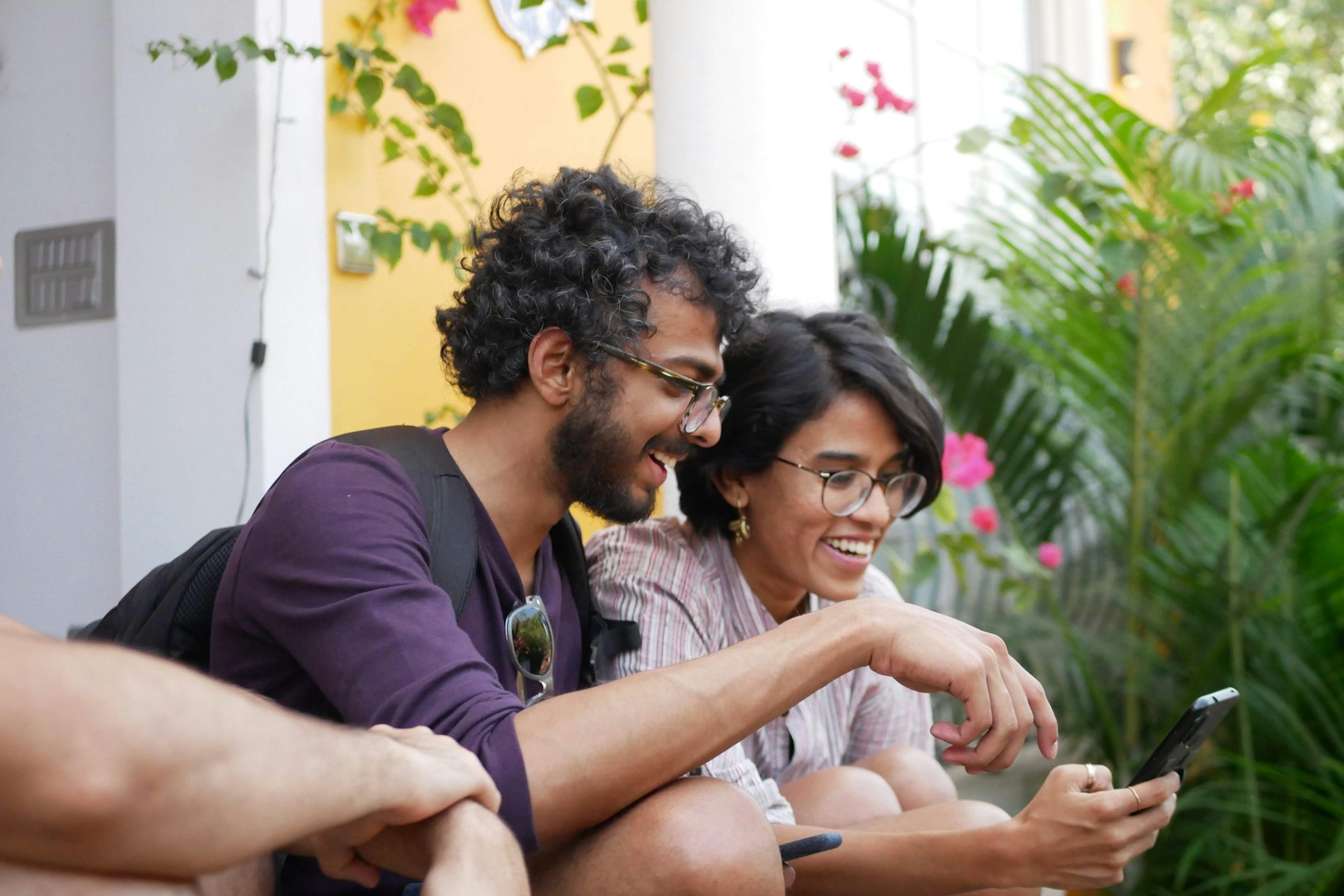 Two friends laughing together while looking at a smartphone outdoors