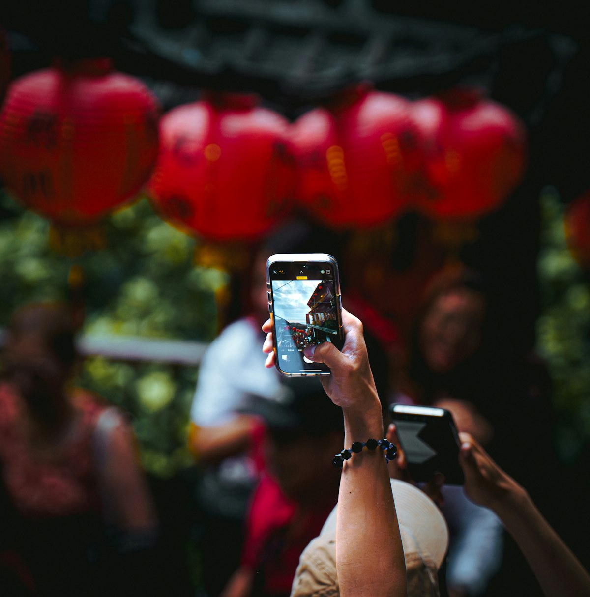 Hands holding smartphones photographing red lanterns at a street festival